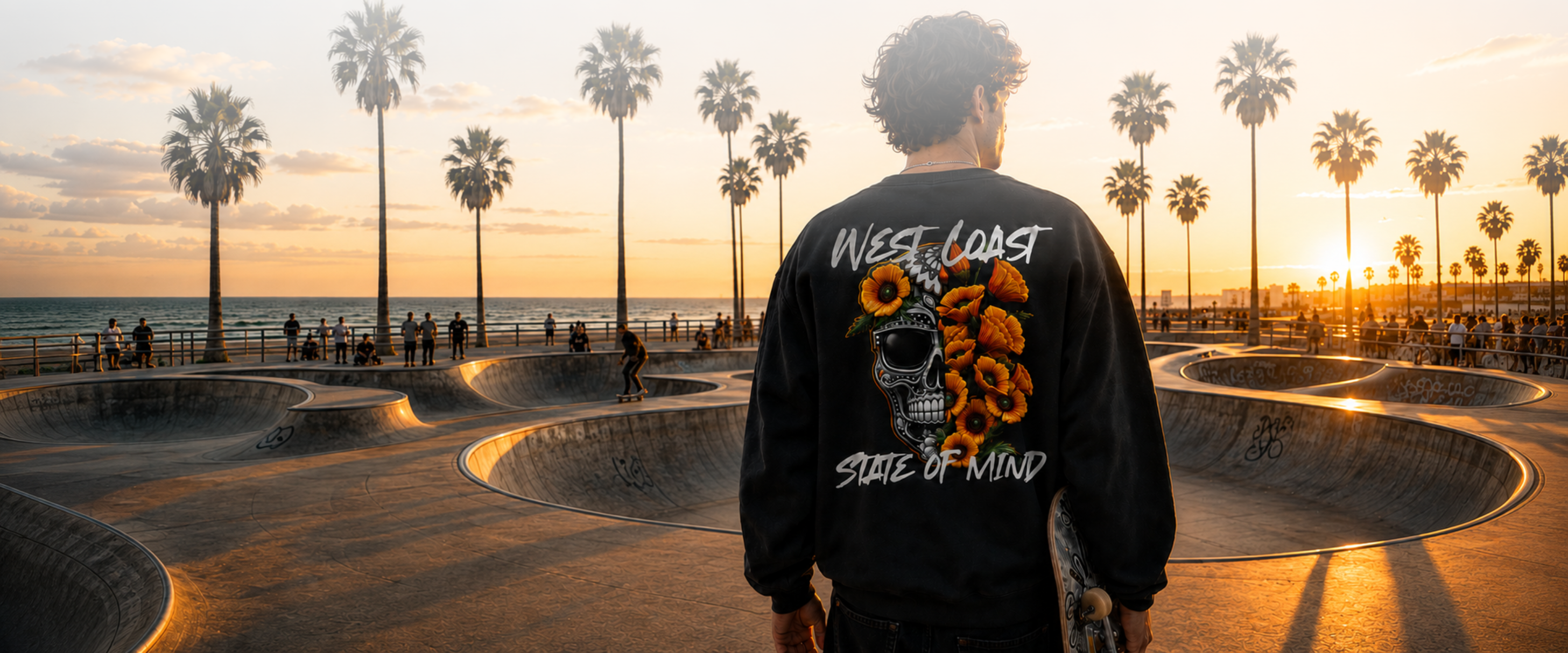 Man wearing CaliPride West Coast graphic hoodie at a California beach skatepark at sunset.